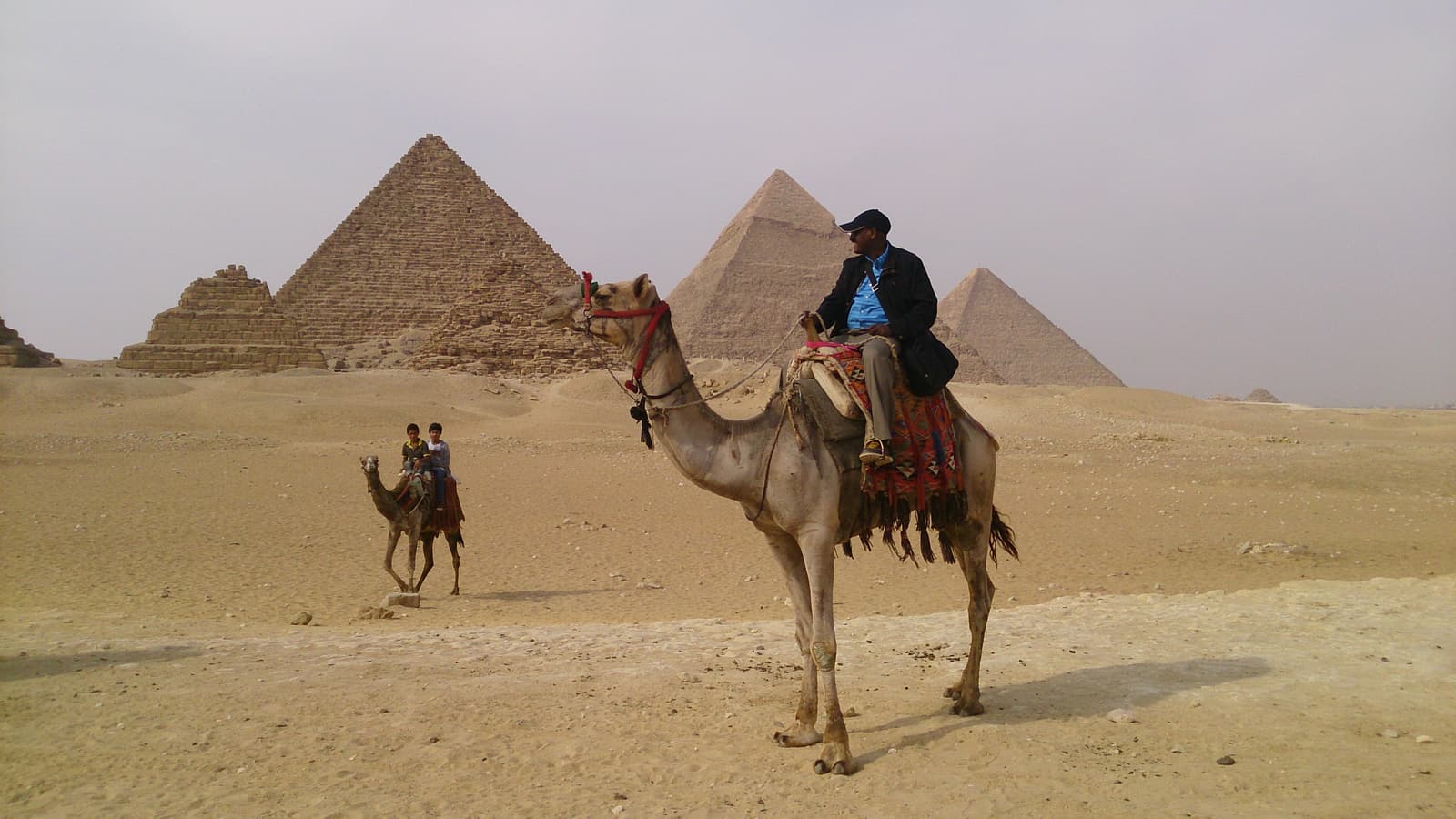 A rider on a camel in the desert with the pyramids of Giza behind
