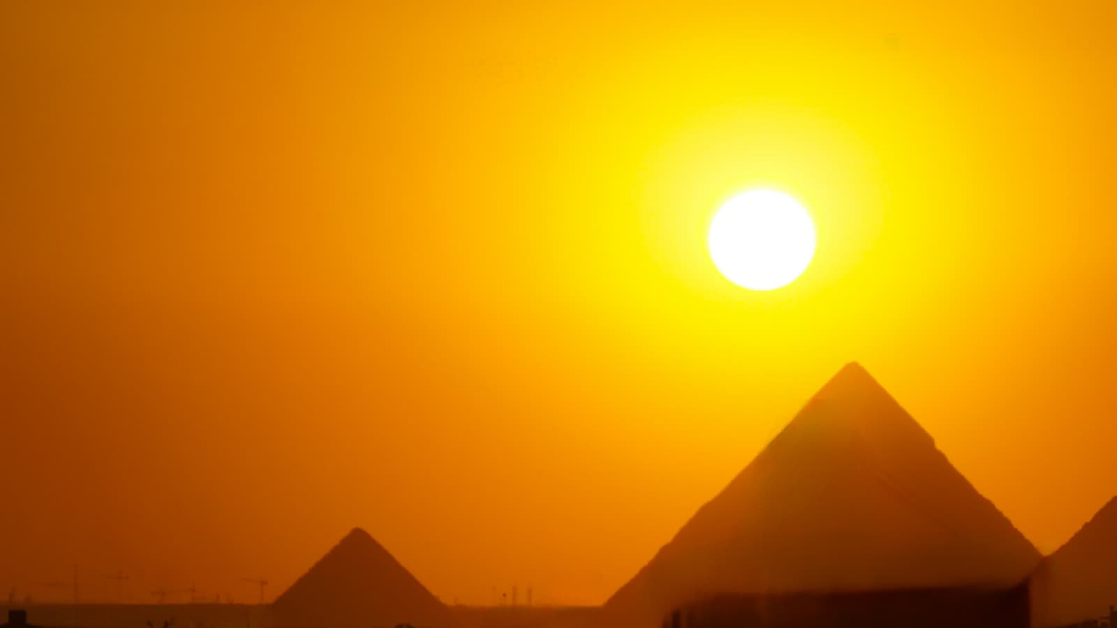 The sun low in an orange sky above the Giza pyramids